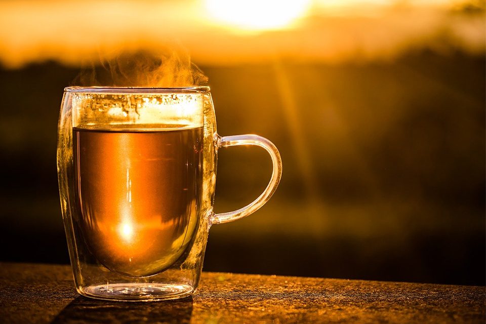 tasse de thé fumante sur fond de coucher de soleil