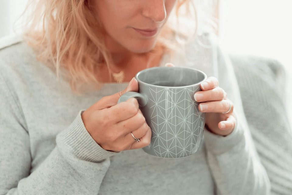 tasse fumante dans mains de femme en pull gris colors of tea