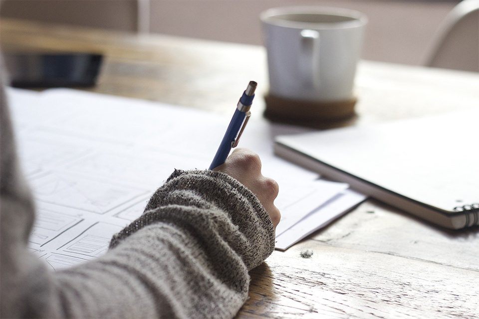 femme qui écrit sur une table en bois avec une tasse femme qui écrit sur une table en bois avec une tasse de thé. Les bienfaits du maté pour la concentration